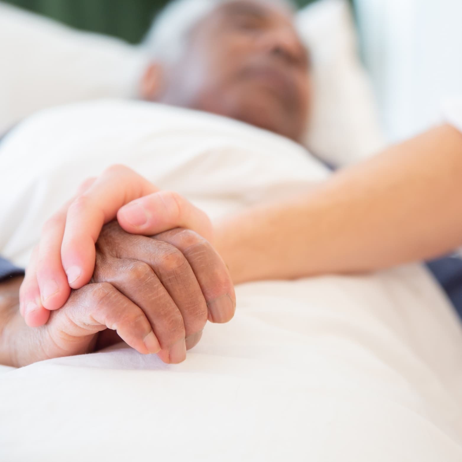 A caregiver holding the hand of an older man resting in bed