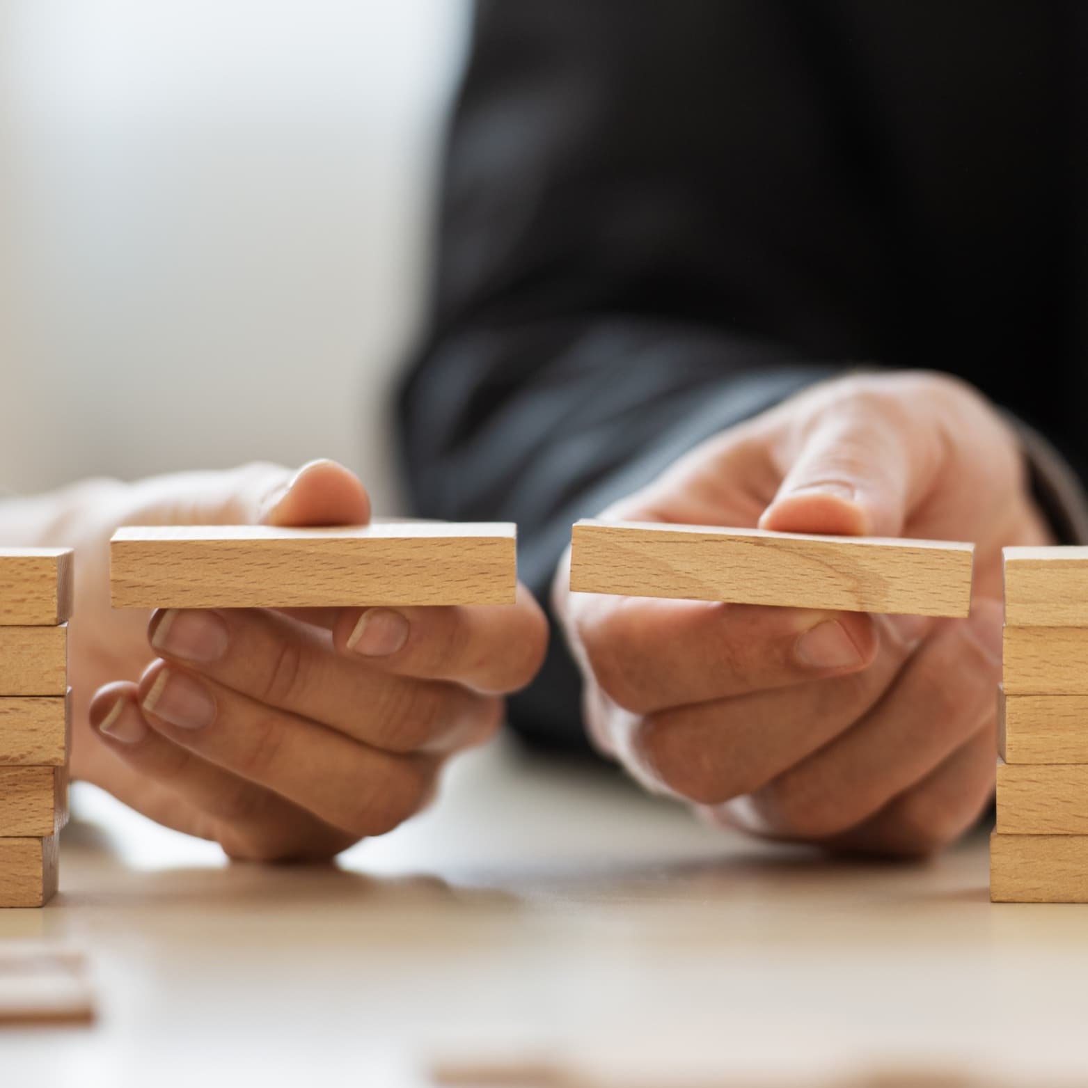 Two hands placing wooden blocks to bridge a gap between stacks