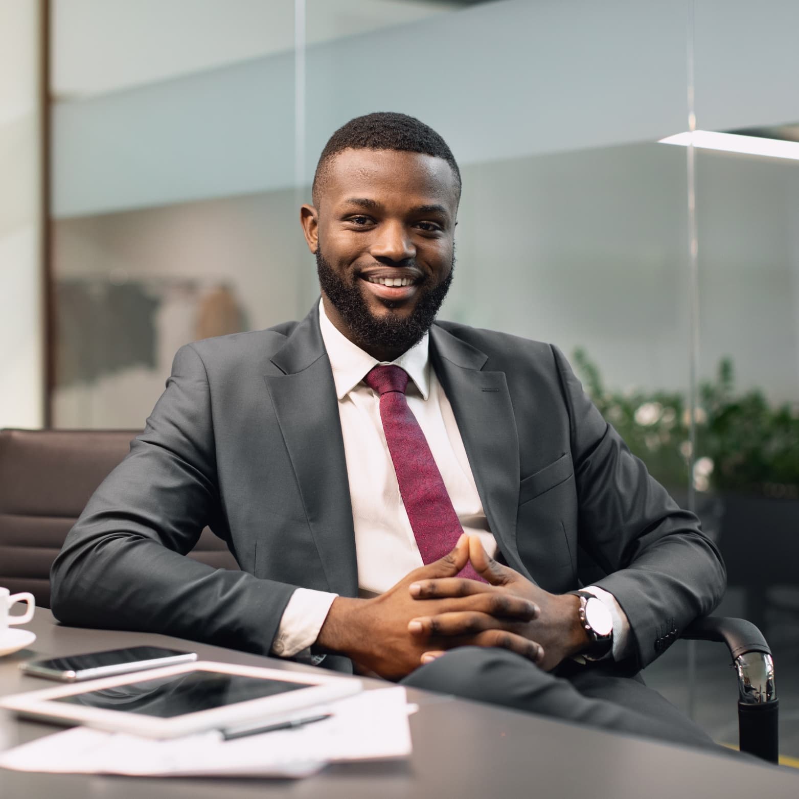 A smiling executive in a dark suit and burgundy tie seated at a conference table